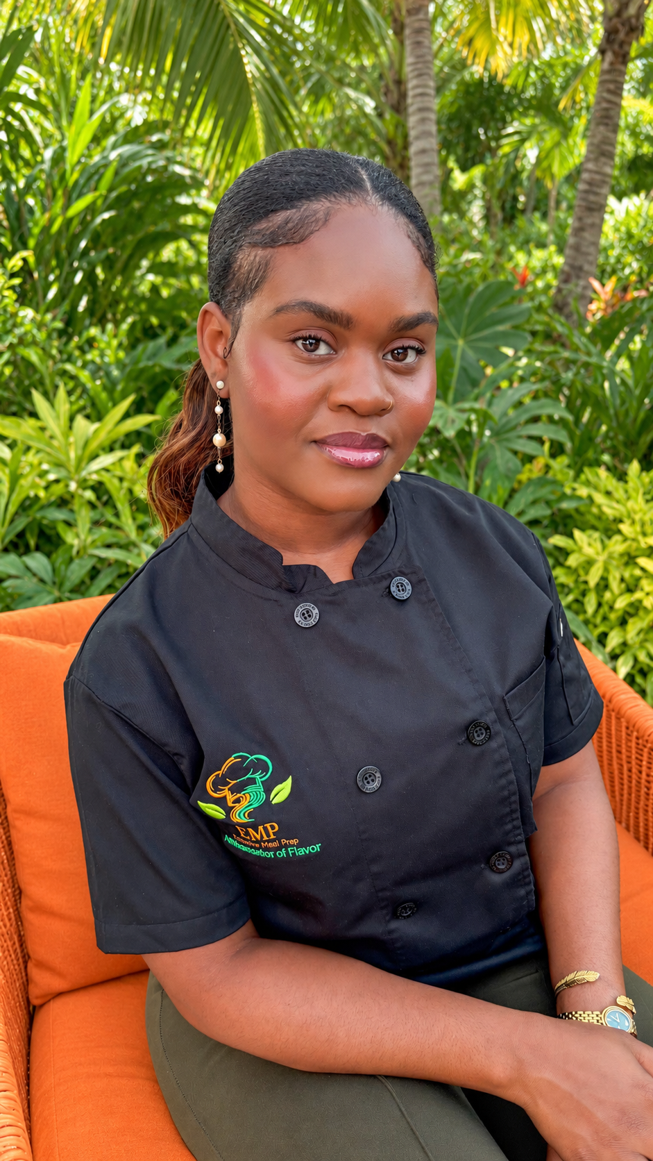 The Ambassador of Flavor seated in a tropical garden, wearing a black EMP chef jacket